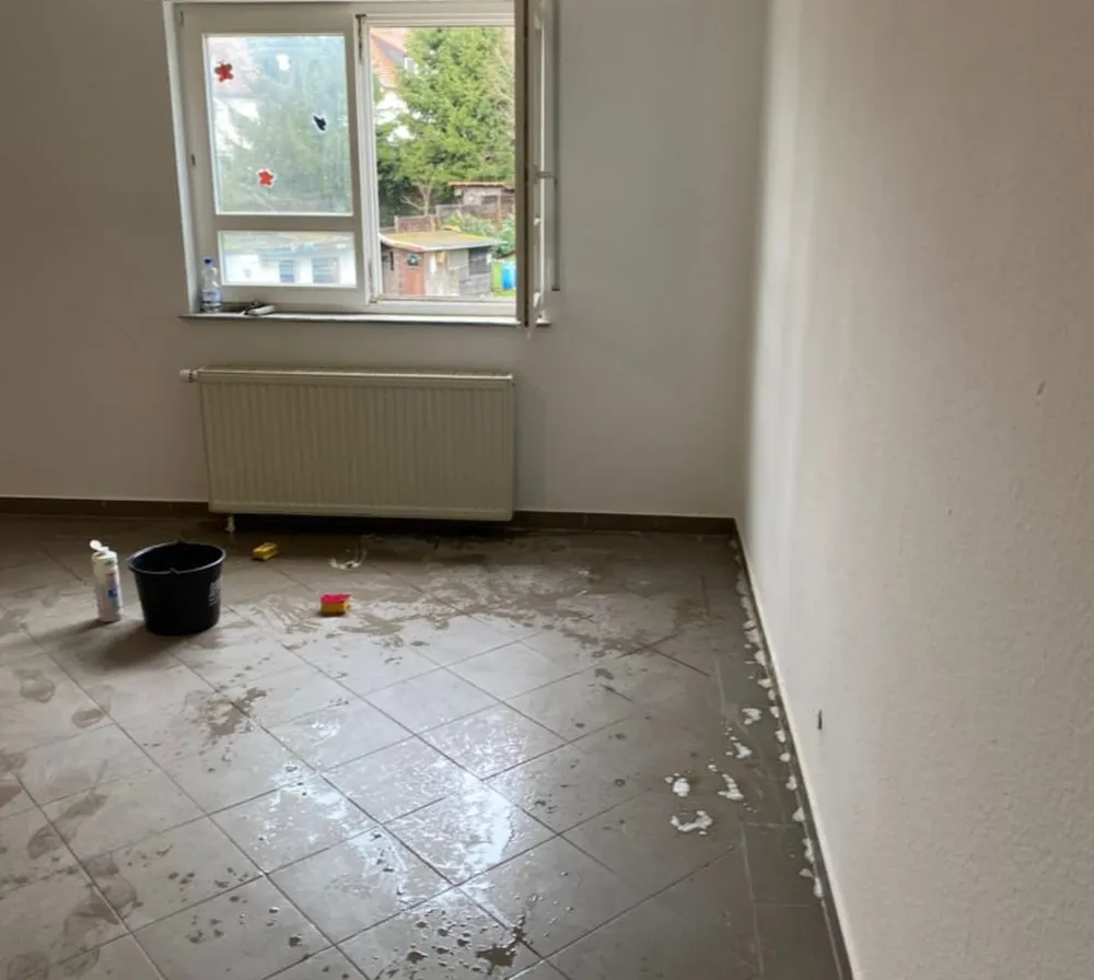 Raum mit fleckigem Fliesenboden und Putzeimer